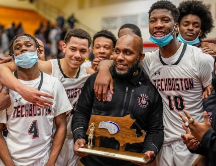 a happy coach holds a trophy surrounded by basketball players 