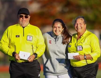 Three adults pose for a photo wearing official gear at a game
