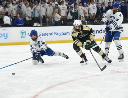 Three hockey players via for the puck during an ice hockey game