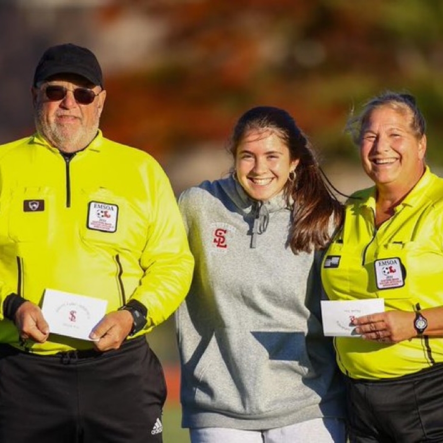 Three adults pose for a photo wearing official gear at a game
